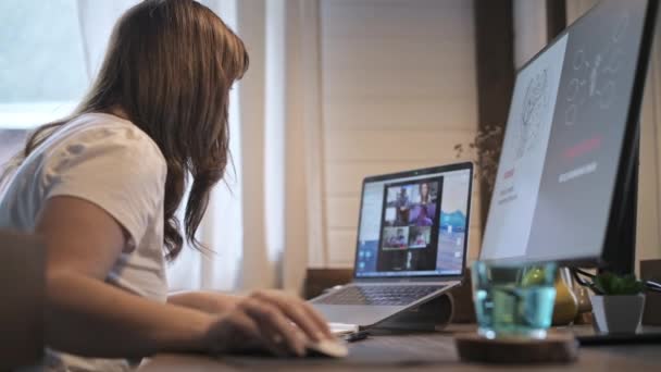 A fiatal, gyönyörű nő egy laptopnál dolgozik. Mosolygó lány tanár ad online leckéket. Üzleti videokonferencia. Iroda otthon. Önelkülönítési körülmények között végzett munka. - Felvétel, videó