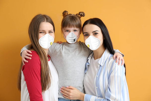 Lesbian couple with little adopted girl wearing protective masks on color background. Concept of epidemic - Photo, Image