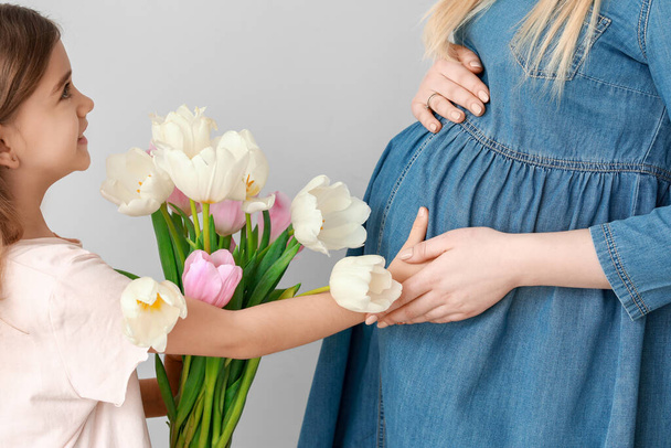 Niña saludando a su madre embarazada con flores sobre fondo claro
 - Foto, Imagen