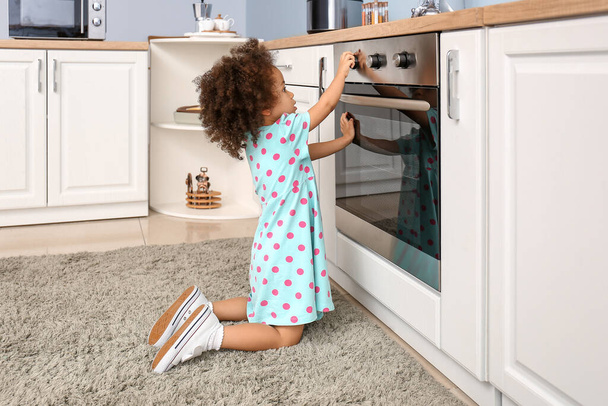 Little African-American girl playing with oven in kitchen. Child in danger - Foto, afbeelding