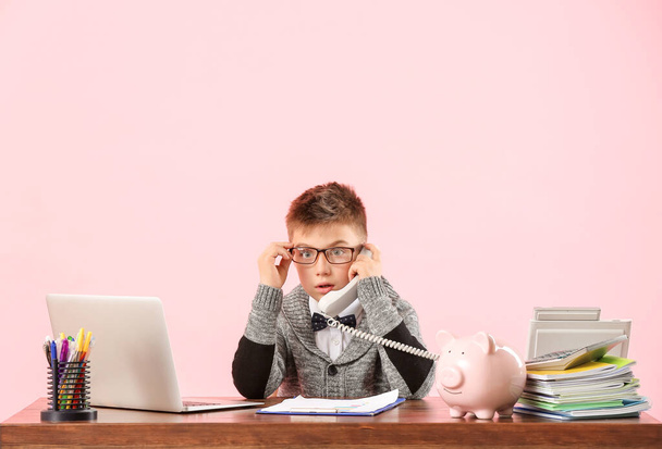 Little accountant talking by telephone at table against color background - Foto, Bild