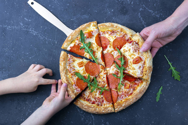 Family snack, mother and child hands taking pepperoni pizza slices. Italian traditional lunch or dinner. Fast food and street food concept. Flat lay, top view, close up - 写真・画像