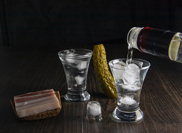 Egy üveg vodkát, két pohár hideg vodkát jéggel, szalonnával és uborkával.. - Fotó, kép