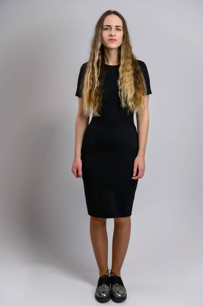 Full-length portrait of a pretty young woman in a black dress with a good figure with long hair. Model stands on a white background. - Φωτογραφία, εικόνα