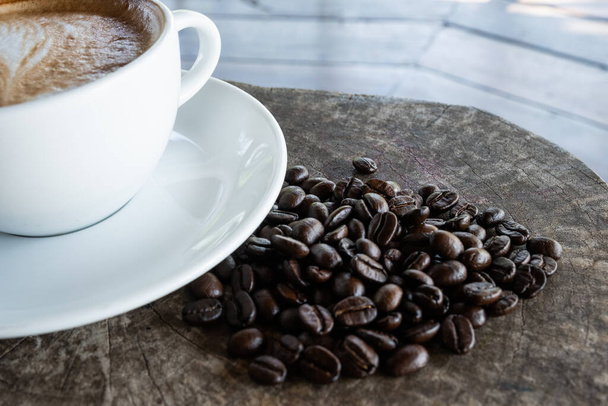 close-up zwarte koffiebonen op een houten achtergrond met witte koffiekop. - Foto, afbeelding