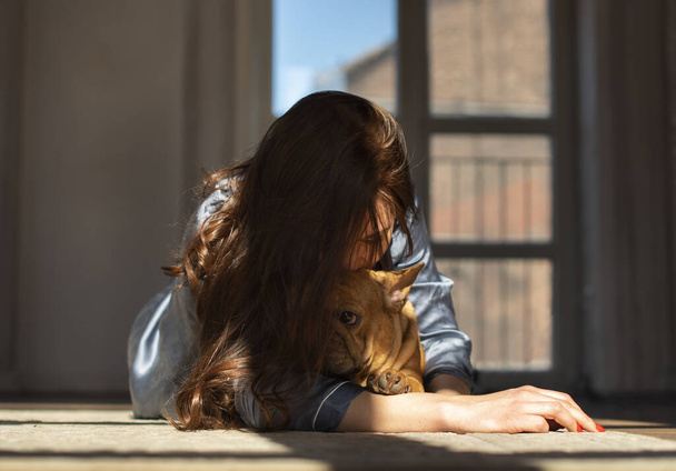 jong meisje en haar hond franse bulldog spelen op de vloer van hun appartement. - Foto, afbeelding