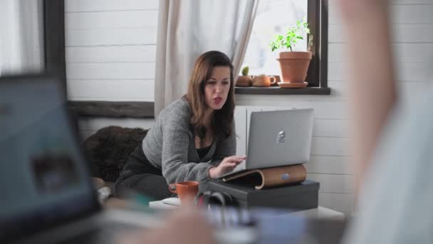 Fáradt beteg lány dolgozik otthonról. Online munka. Szabadúszó távolról dolgozik. Egy fiatal nő dolgozik egy számítógépen egy asztalnál otthon. Köhögés és a betegség első jelei. - Felvétel, videó
