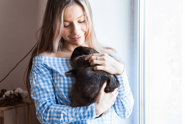 Концепція "Кішка і Великдень" - приваблива дівчина обіймає коричневого кролика вдома
. - Фото, зображення