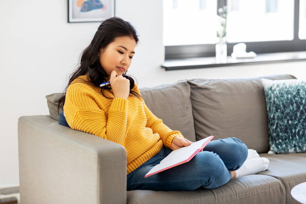 asian woman with diary sitting on sofa at home - Foto, afbeelding