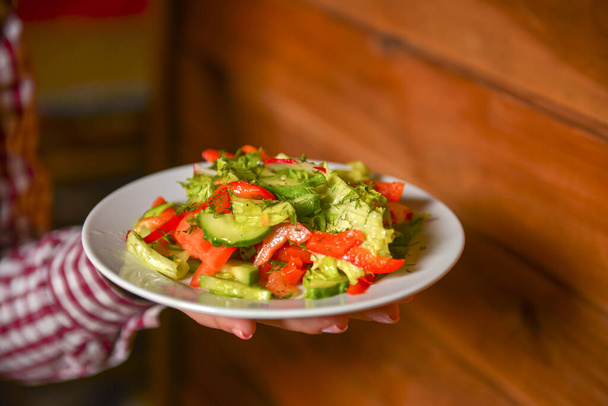 Waiter serving vegetable salad with juicy tomatoes, lettuce, radish, cucumber. Restaurant service. - Photo, Image