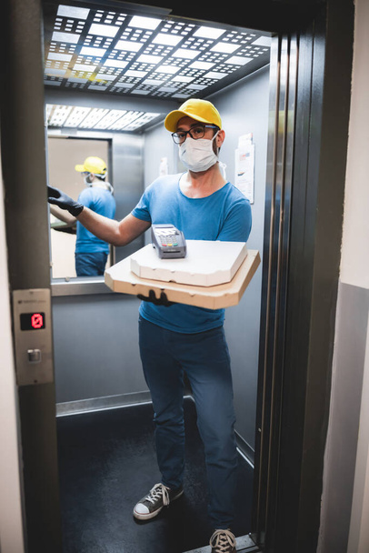 Doručovatel s ochrannou lékařskou maskou drží pizza box a POS bezdrátový terminál pro platby kartou - dny virů a pandemie, dodávky potravin do vašeho domova. - Fotografie, Obrázek