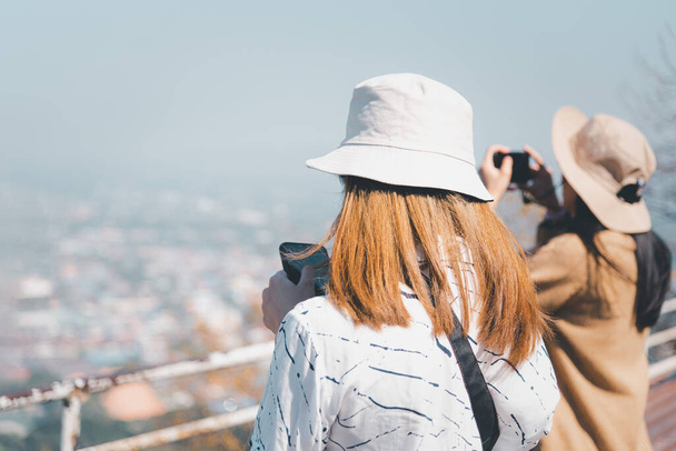 アジアのかわいい女性の帽子はリラックスし、山の上の海辺の都市景観の視点でスマートフォンを使用し、コンセプト旅行、休暇、生活の中でのレジャーで幸せと自由の感情 - 写真・画像