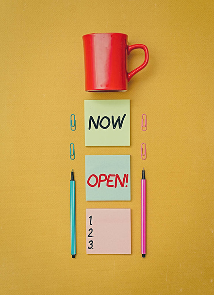 Handwriting text writing Now Open. Concept meaning leave door or windows not closed or barred at this current time Coffee cup blank colored sticky note two ballpoints clips yolk background. - Photo, Image