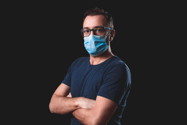 Adult person with protective face mask posing on a black background - social issues with virus and hygiene safety measures. - Photo, image