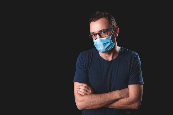 Adult person with protective face mask posing on a black background - social issues with virus and hygiene safety measures. - Photo, Image