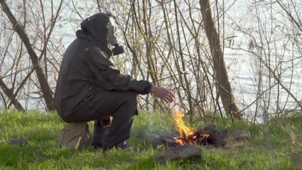 Mężczyzna w masce gazowej smaży kiełbasę przy ognisku. - Materiał filmowy, wideo