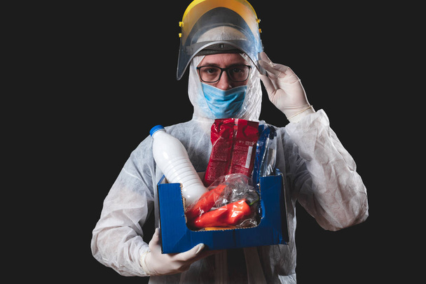Food and groceries home delivery, pandemic outbreak hysteria, person in a full protective suit uniform holding a box with supplies. - Photo, Image