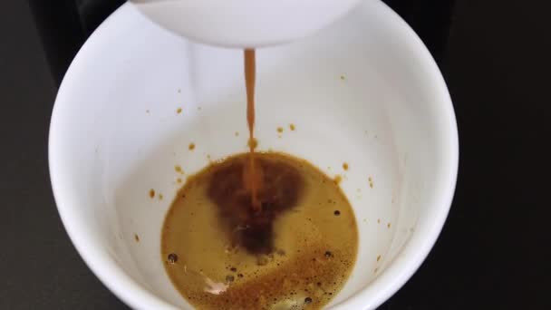πρώτα δευτερόλεπτα ζυθοποιίας μαύρου καφέ espresso σε ένα λευκό κύπελλο με μια καφετιέρα σε μαύρο φόντο, αργή κίνηση - Πλάνα, βίντεο