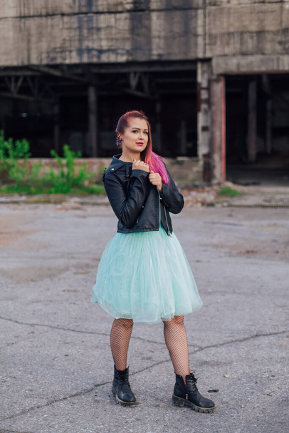 Portrait of a young girl with pink hair dressed in leather jacket and a blue skirt standing outside of collapsed building - Fotoğraf, Görsel