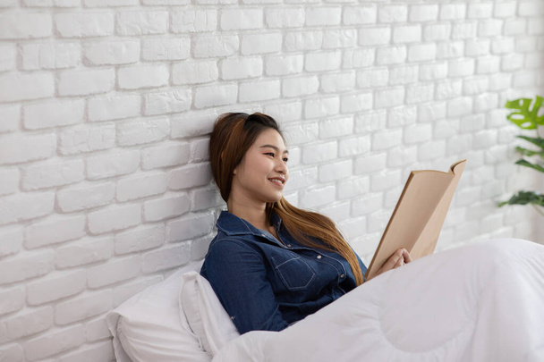Beautiful Attractive Asian woman sitting on bed in cozy bedroom reading book for learn and education smile and positive thinking feeling so happiness and comfortable,Education Concept - Zdjęcie, obraz