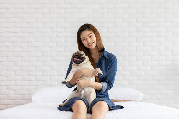 Beautiful Asian young woman playing with her dog and smile with dog pug breed looking in funny and serious face in bedroom feeling so happiness and relaxation,Dog Friendship Concept - Fotografie, Obrázek