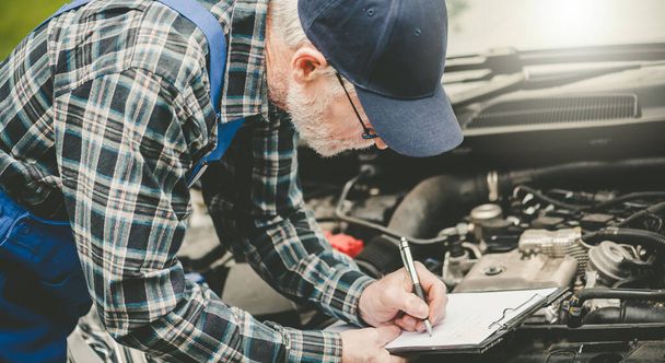 Автомеханик проверяет двигатель автомобиля и пишет на планшете - Фото, изображение