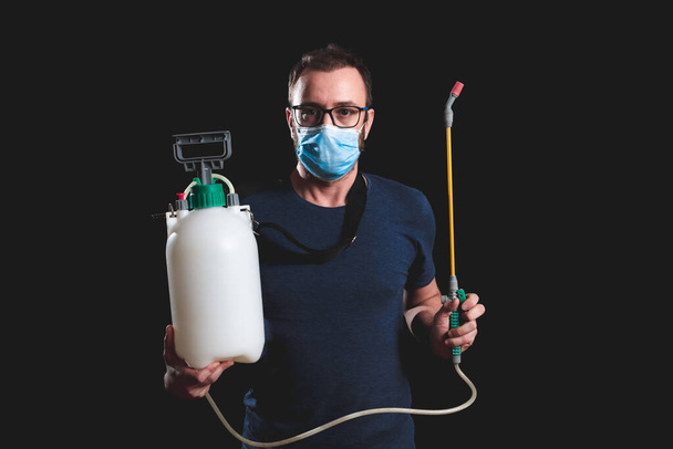 Persona con maschera antivirale protettiva, bottiglia dello spruzzatore di decontaminazione chimica nell'isolamento domestico
. - Foto, immagini