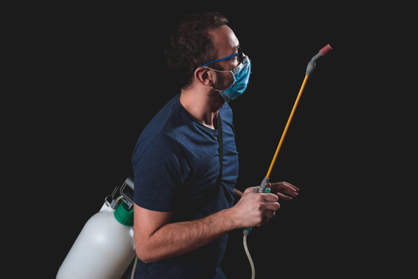 Πρόσωπο με προστατευτική αντιική μάσκα, φιάλη ψεκαστήρα χημικής απολύμανσης στο σπίτι απομόνωση. - Φωτογραφία, εικόνα