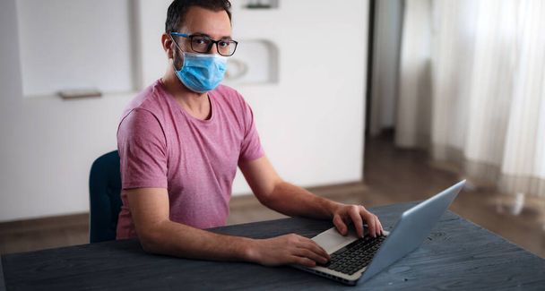 Libero professionista con maschera protettiva medica che lavora da casa nei giorni di pandemia e distanza sociale
. - Foto, immagini