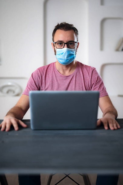 Freelancer with medical protective mask working from home in the days of pandemic and social distancing. - Photo, Image