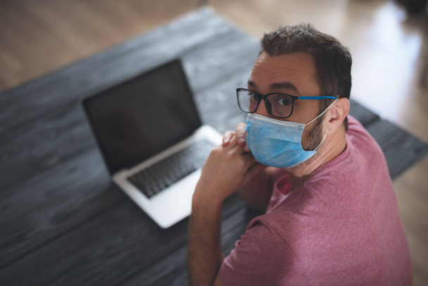 Фрилансер в медицинской защитной маске, работающий из дома в дни пандемии и социального дистанцирования
. - Фото, изображение