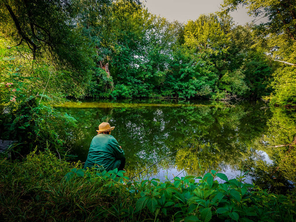 vrouw in een stro hoed vissen vroeg in de morgen in een rustige groene bos - Foto, afbeelding