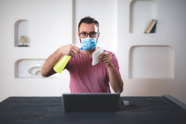 Homme avec pulvérisateur chimique travaillant sur un ordinateur portable de la maison
. - Photo, image