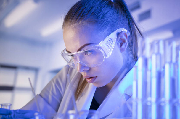 Tudományos kutatási koncepció. Fiatal tudós a kísérlet során és mikroszkóppal a modern laboratóriumban. Üvegcső és főzőpohár. - Fotó, kép