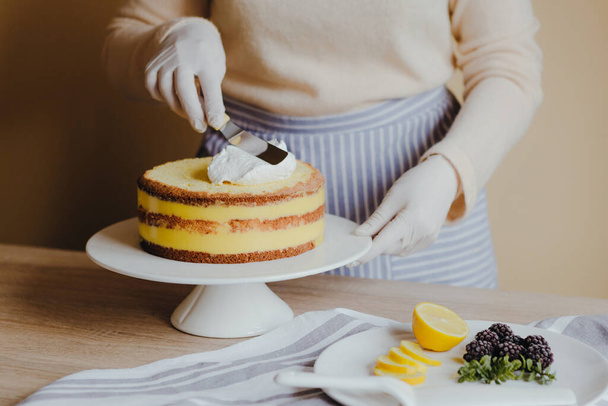 Ama de casa en la cocina cocinando un pastel de limón con frutas, mora, limón y menta sobre fondo amarillo durante la cuarentena. Receta de pastel de limón casero orgánico. Cocinar en casa
. - Foto, Imagen
