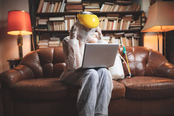 Mujer con máscara antiviral protectora y uniforme usando portátil en casa, trabajando, leyendo noticias, navegando por Internet, pidiendo comida en línea
. - Foto, Imagen