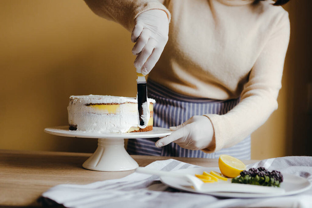 Gospodyni domowa rozsypuje lukier, żeby przykryć tort. Gospodyni domowa wygładza powierzchnię szpachelką, zamyka przycięte zdjęcie. Czas wolny na kwarantannę. - Zdjęcie, obraz