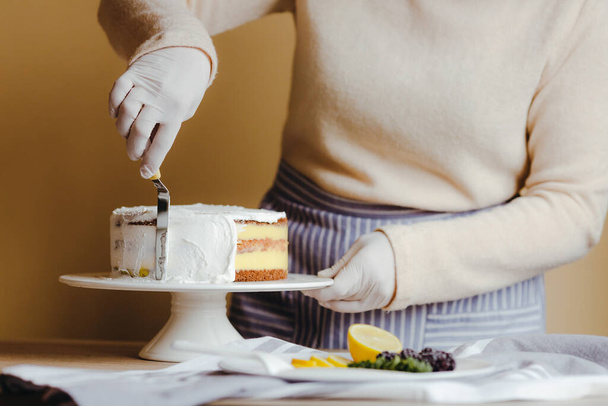 Žena v domácnosti roztahuje polevu, aby zakryla vršek dortu. Žena v domácnosti vyhlazuje povrch stěrkou, zblízka oříznutá fotka. Volný čas v karanténě. - Fotografie, Obrázek