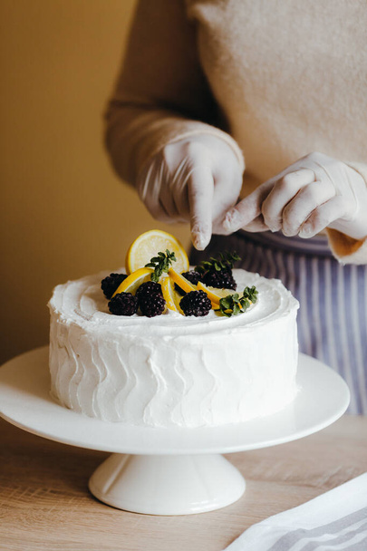La casalinga in cucina decora una torta al limone con frutta, mora di rovo, limone, menta durante la quarantena. Ricetta di torta di limone fatta in casa biologica
 - Foto, immagini