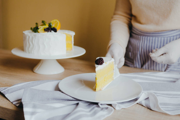 Νοικοκυρά λαμβάνοντας φέτα από φρέσκα νόστιμα γενέθλια σπιτικό κέικ λεμονιού στο τραπέζι, top view. Συνταγή του λεμόνι βιολογικό κέικ. - Φωτογραφία, εικόνα