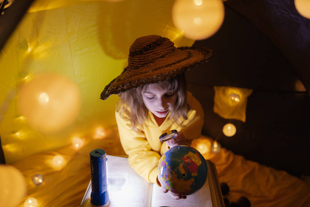 Νεαρή κοπέλα μαθαίνοντας και homeschooling σε μια σπιτική σκηνή με λαμπερό φως μπάλες. - Φωτογραφία, εικόνα