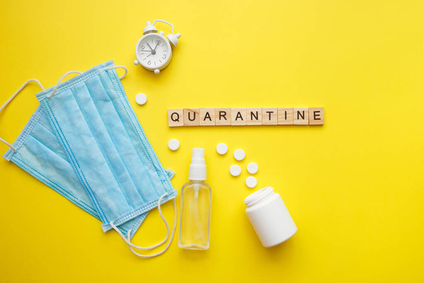 Top view of a yellow background with the word quarantine. Protective medical mask, alcohol spray and pills. Respiratory syndrome. World quarantine concept. - Foto, immagini