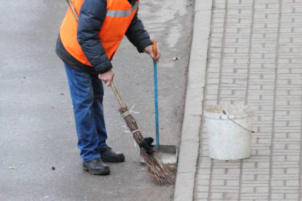Close up janitor men in an orange uniform jacket sweeps the paved street road with a broom, top side view - Foto, Imagem