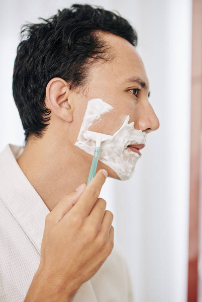 Handsome man shaving in bathroom after taking shower - Фото, зображення