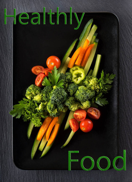 Caption - Healthy food on a black plate with fresh vegetables - broccoli, cucumbers, and tomatoes - Foto, afbeelding