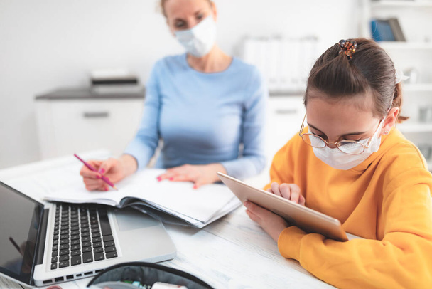 Child home studying education, homeschooling, with private tutor / mother with protective mask in the time of viruses, flu and seasonal pandemic, healthy approach in social contact. - Foto, imagen