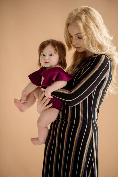 Young mother blonde with baby in fashionable outfit in studio beige background - Foto, afbeelding