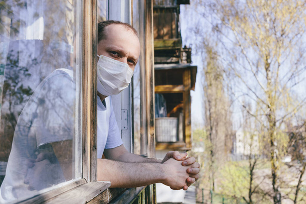 Un hombre con máscara protectora en el balcón. Coronavirus pandémico 2020. Cuarentena. Concepto de virus. Infección epidémica
.  - Foto, imagen