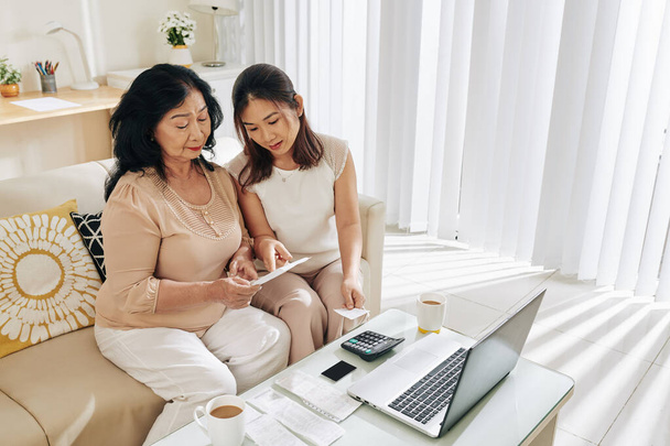 Mujer asiática joven ayudando a su madre mayor a averiguar cómo pagar la factura en línea a través de la computadora
 - Foto, imagen