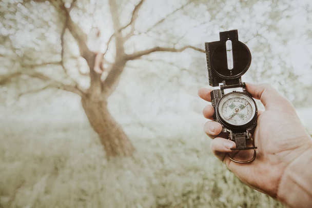 Compass in hand against light coloured nature background with old dry tree grass and bright sunshine - Photo, Image